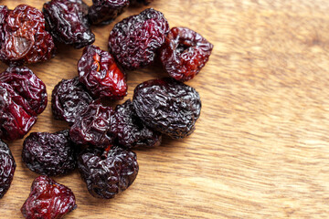 Dried cherries scattered on a wooden surface. Wrinkled dark red fruits. Healthy berries rich in antioxidants. Prunus avium. Close-up.