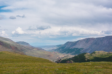 Dramatic top view from green pass through sunlit forest hills to wide alpine valley between large...