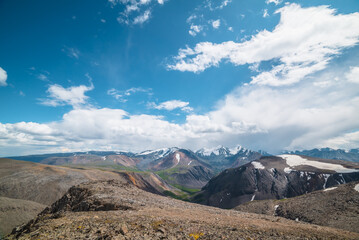 Awesome top view from precipice edge to snow-covered mountain range with several snow-capped peaked tops in sunlight. Scenic alpine landscape with few big snowy pointy peaks under clouds in blue sky.