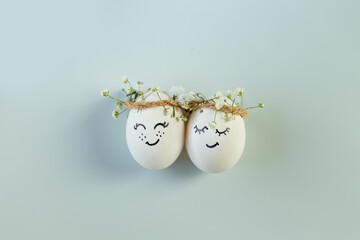 Two chicken eggs with hand drawn happy faces with wreaths on light blue background.