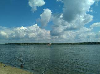 Summer evening landscape with beautiful clouds over the river, the edge of the shore with 2 fishing rods