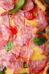 Pizza closeup texture, food pattern background. Ham, tomatoes, green basil leaves and cheese. Top view