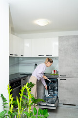 Woman using dishwasher in the kitchen. Household and smart technology concept. High quality photo