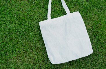 Eco friendly concept with white canvas tote bag on the green lawn background.