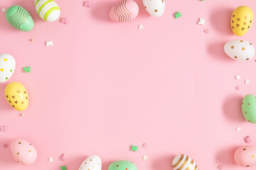 Decorative Easter eggs in beautiful patterns and sugar candies with empty space for text on a pink background. Top view
