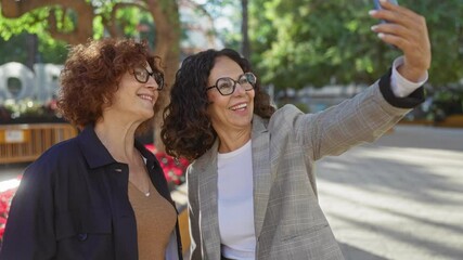 Women taking selfie in urban park setting, showcasing friendship and joy amidst vibrant greenery and cityscape, embodying cheerful connection and outdoor leisure.