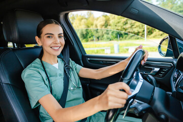 Smiling beaming young woman in scrub suit driving a car