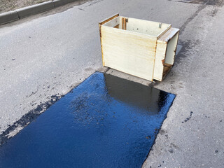 Road repair details. Fall asleep with hot asphalt or bitumen pits on the road. Fence made of improvised means, a wooden box instead of warning signs.