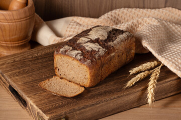 Freshly baked whole grain bread resting on a wooden cutting board with woven cloth and wheat stalks nearby