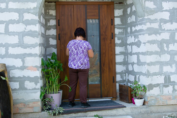 A woman in a purple floral shirt stands at the entrance, facing a wooden front door. The entrance...