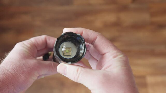 A metallic flashlight held in hands, with a power button on the body