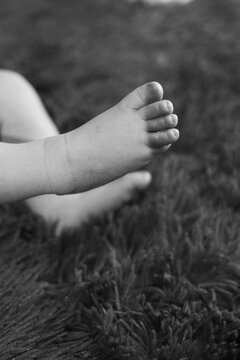 black and white shot that focuses on the baby's leg. The small baby's foot is raised up against the background of a soft, fluffy covering. The tenderness and defenselessness of the baby. 