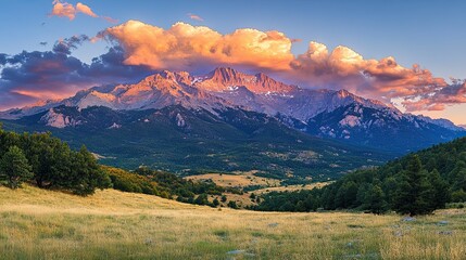 A dramatic mountain range at sunset, with clouds swirling around the peaks and a golden glow.