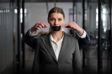 Businesswoman in a suit with mouth covered by black tape, controlled by hands behind her,...
