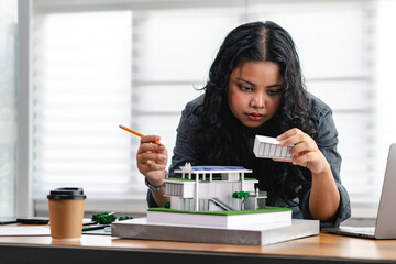Young architect or design student holding part of house model while thinking about sustainable design, double glazed windows and adding natural light for Eco House design project with home models.