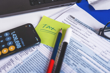 Tax form 1040, w-9, pencil, marker pen, reading glasses and laptop are laying on accountant's desk