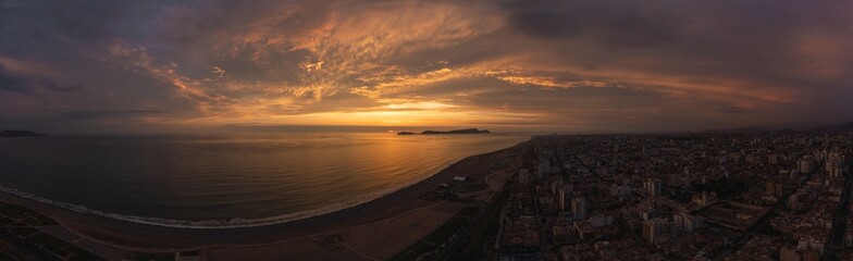 Sunset illuminating coastline and cityscape with dramatic clouds, Panoramic view