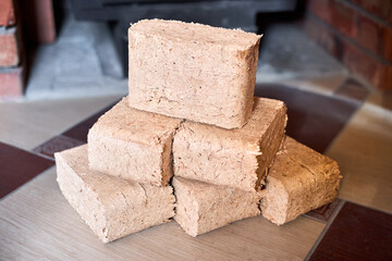 Fuel briquettes made of ruf type made of birch and oak alternative eco-friendly fuel for the fireplace in the house. Fuel briquettes lay near steel stove with tiled floor cottage interior.