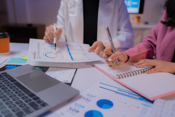 Businesswomen collaborating in an office, analyzing financial documents and charts, pointing out...