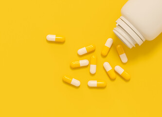 Vitamin supplements. White and yellow medications poured out white plastic bottle on yellow background. Color image with space for text.