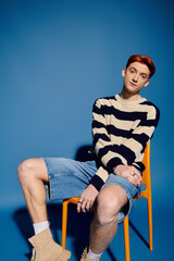 Emotional expression of a young handsome man sitting casually against a bold blue backdrop