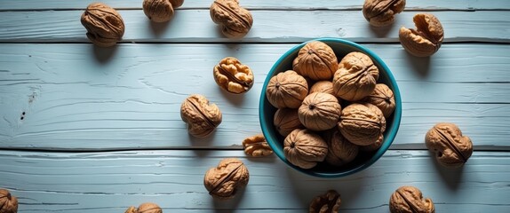 Fototapeta premium Fresh walnuts in a blue bowl on rustic wooden surface with scattered nuts creating a natural and appetizing composition.