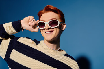 Young handsome man expressing joy in stylish sunglasses against a vibrant blue backdrop