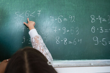 A child's hand points to a chalkboard with math problems, highlighting education. The scene...