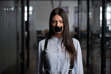 Young woman with long hair and closed eyes standing in an office corridor with black tape covering...