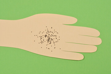 A top-down shot of a paper cutout of a hand against a green background, with numerous tiny black...