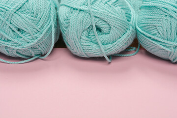 A close-up, low-angle shot of three skeins of light blue yarn arranged in a row against a pink surface, emphasizing the texture and softness of the yarn