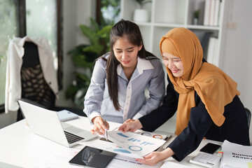 Diverse businesswomen collaborating over financial reports and laptop in a modern office, discussing strategy.