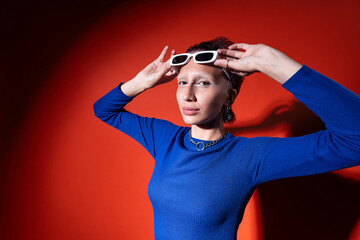 Trendy Woman in Blue Top Posing with Sunglasses on Red Background
