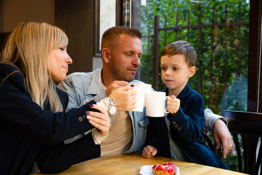 Mom, dad and their little son have tea party breakfast at a table in a bakery, eat sweet donuts and talk. Happy family concept. Weekend time