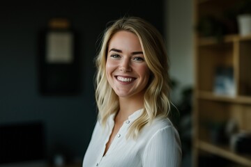 Headshot portrait of a cheerful young businesswoman with blond hair smiling in a modern office environment, conveying confidence and professionalism