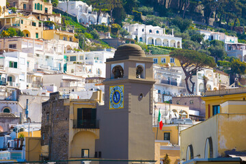 Clock tower in Piazza Umberto, knows as La Piazzetta, Capri, Italy, stands against backdrop of Mediterranean-style buildings with white and pastel facades