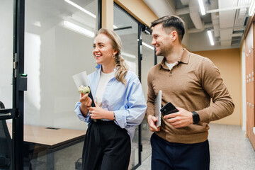 Colleagues enjoy casual conversation while walking in modern office space with snacks in hand