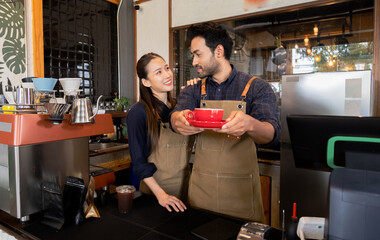 Cafe small business entrepreneur couple presenting coffee with red cup. Male and female baristas with aprons standing behind counter with coffee machines. startup restaurant owner in cozy workplace
