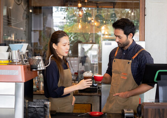 Two baristas couple exchanging drinks behind coffee counter. Asian female and Indian male holding hot drink. family small business startup in cozy cafe restaurant, coffee tasting before opening shop