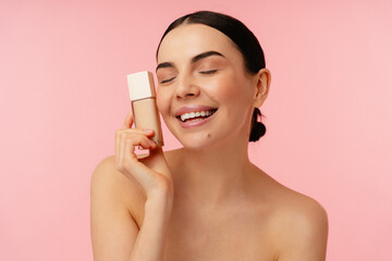 Joyful individual showcasing facial foundation while radiating confidence and beauty on a pink...