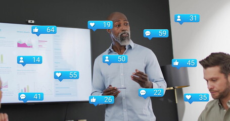 Image of media icons over diverse colleagues discussing work in office