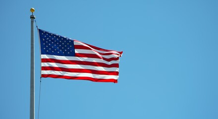 Fototapeta premium American Flag Waving Proudly Against a Clear Blue Sky Background