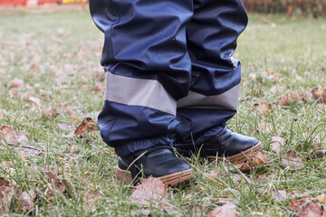 Close up of toddles feet on frozen green grass ground wearing warm outwear clothes and playing outdoors 