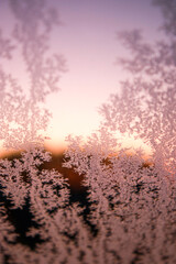 Close up of a frosty window with blurry pink sunrise in background. Nature beauty pattern texture 