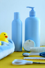 Photo of skin care products on a yellow and white background. With a bright rubber duck.Also in the photo are combs, nail scissors and a toothbrush.Blue and white robe for baby