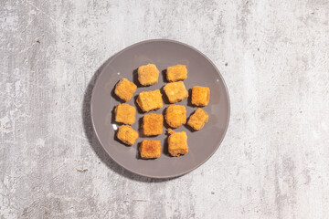 A grey plate with multiple pieces of crispy breaded tofu, placed on a textured grey background, ready to be served.