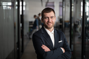 Confident businessman, manager or executive in a suit standing with arms crossed in a modern...
