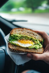 A man eating an avocado and egg sandwich while driving, with the sandwich wrapped in a thick napkin for convenience. The bread is toasted on both sides, with  egg inside,  yolk ,Creamy avocado 