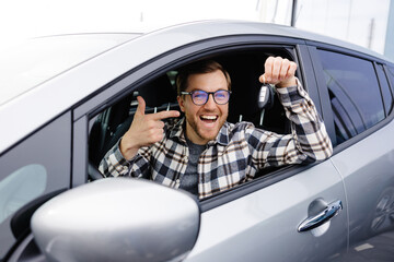 Excited young man showing a car key, sitting inside his new vehicle
