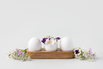 White eggs in wooden stand with spring pear and strawberry, purple viola flowers on a gray background. Happy Easter